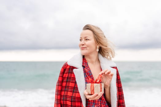 Lady in plaid shirt holding a gift in his hands enjoys beach. Coastal area. Christmas, New Year holidays concep