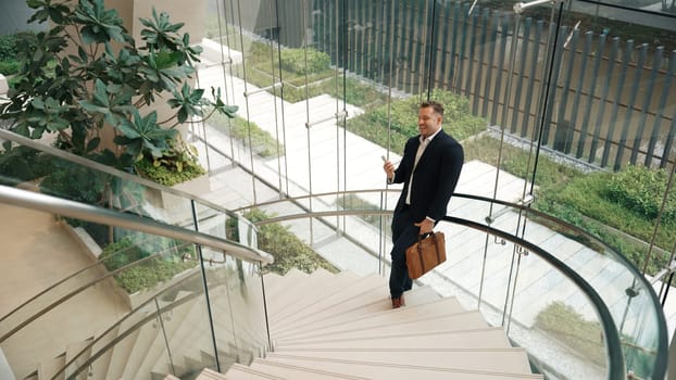 Caucasian businessman analyzing marketing data from mobile phone and making decision at modern glass wall building. Happy project manager checking start up project sales report while standing. Urbane