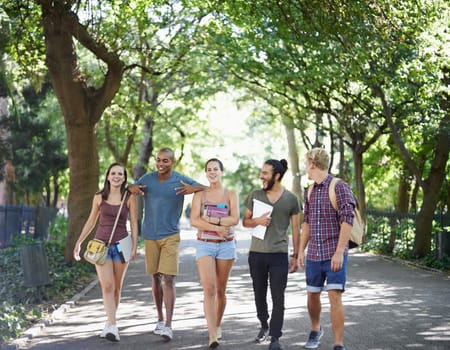 Students, friends and walking on campus with learning, knowledge and books or talking of college. Group of people with outdoor conversation in a park or university for education, study or opportunity