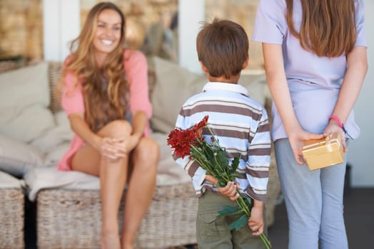 Mothers day, surprise and home with children, flowers and back together with a hug, gift and holiday. Family, girl and mom excited on a living room sofa with a present and floral bouquet in house