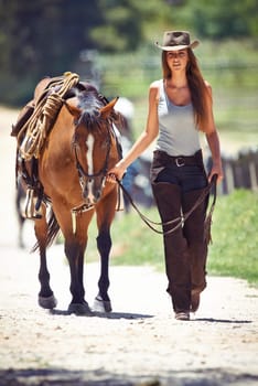 Woman, portrait and cowgirl walking with horse in countryside for ride, journey or outdoor adventure in nature. Female person or western rider with hat, saddle and animal stallion at ranch or farm