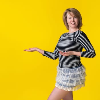 Portrait of blondie in mini skirt and striped long sleeve pointing to space for future advertising