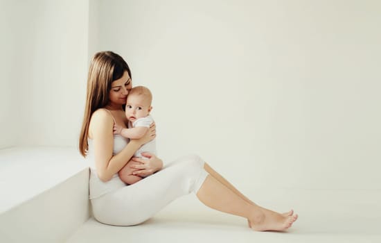 Happy young mother holding cute baby together in white room at home