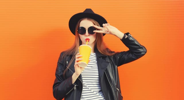 Portrait stylish young woman drinking juice posing in black rock style leather jacket, round hat