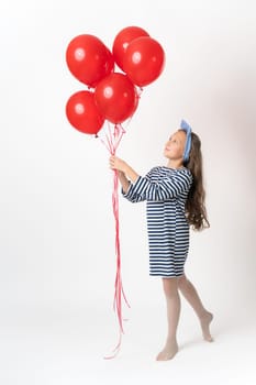 Nosy girl holding bunch of red balloons in two hands and looking at balloons on white background
