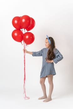 Girl in striped dress holding large bunch of red balloons on outstretched hand and looking at them