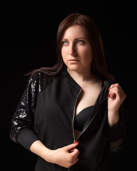Shy brunette woman unzipping black jacket and showing bra, looking up away. Waist up portrait