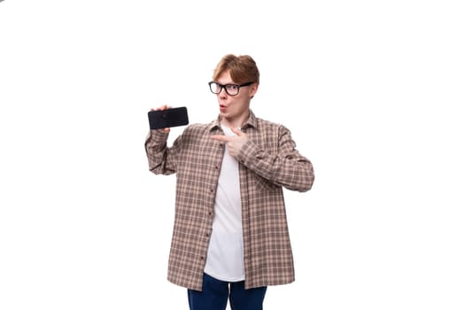 young stylish man with red hair dressed in a summer shirt shows a phone with a mockup