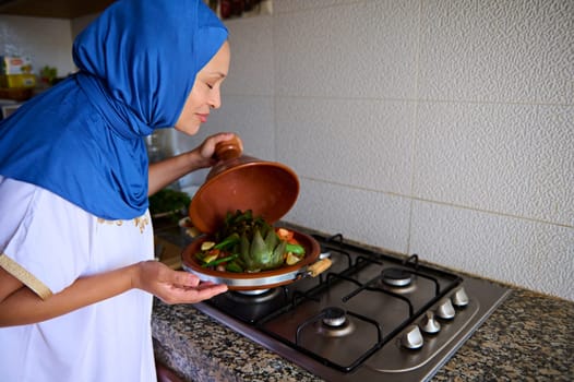 Moroccan housewife cooking vegetables in tagine clay dish at home kitchen