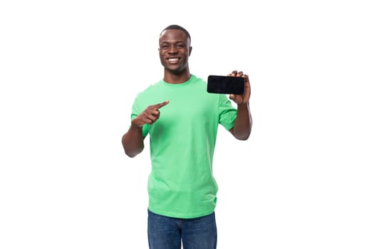 30 year old cool stylish african man dressed in a light green t-shirt and jeans holds a smartphone with a mockup