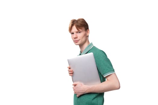 young positive red-haired caucasian guy in a green t-shirt works as an IT specialist and owns a laptop