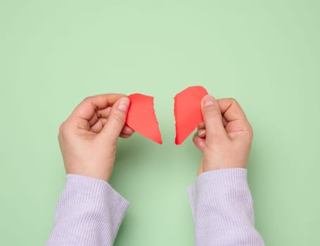 Two female hands tearing a red paper heart, symbolizing divorce 