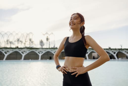Smiling woman in sportswear have a rest after workout outside standing on building background
