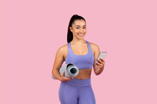 Smiling young woman with yoga mat and smartphone
