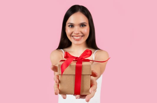 Happy young european woman offering gift box with red ribbon