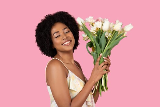 Radiant woman with a natural afro hairstyle blissfully embracing a bunch of fresh white tulips