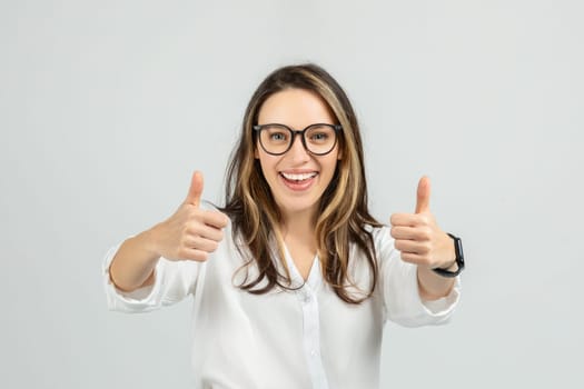 A smiling young woman with long hair and glasses gives two enthusiastic thumbs up