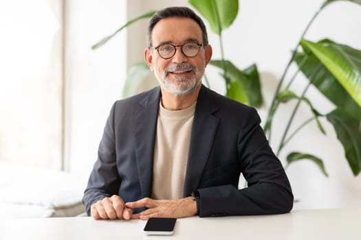 Confident mature businessman with glasses, smiling and sitting at a white table