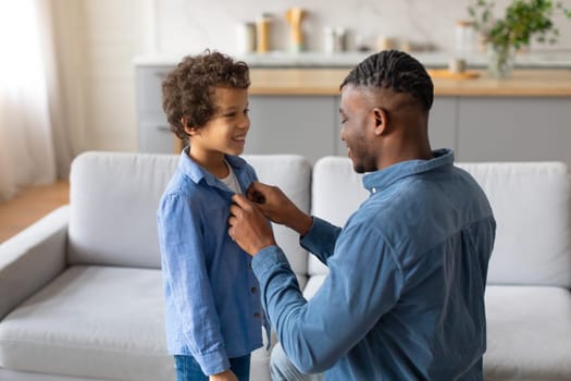 Young black father adjusting son's shirt, both smiling warmly
