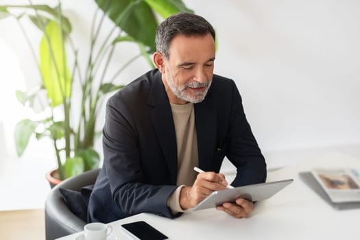 Focused mature businessman in a smart suit working intently on a tablet with a stylus