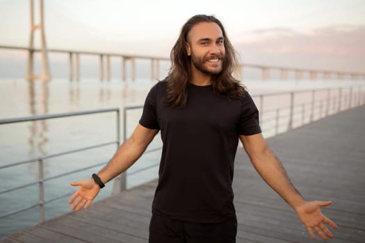 Sporty long haired man spreads arms wide by sea outdoor