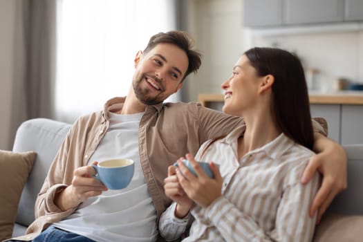 Happy european couple enjoying coffee on couch and chatting