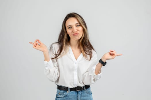 A young woman wearing a white blouse and blue jeans with a smartwatch makes an uncertain expression