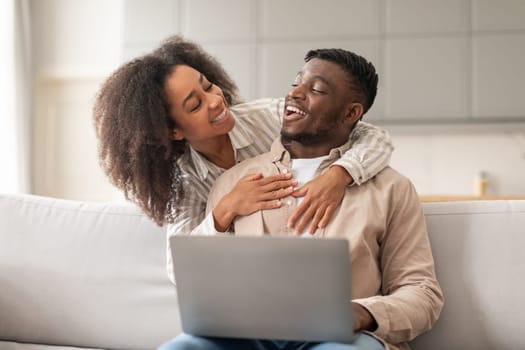 Young African American couple hugs watching movie on laptop indoor
