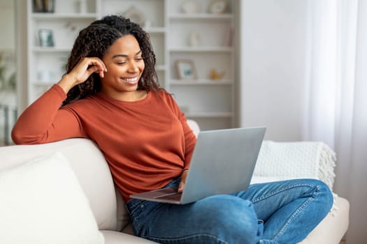 Smiling Black Female Relaxing With Laptop On Couch At Home