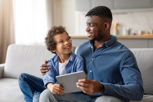African american father and son sharing digital tablet, looking happy