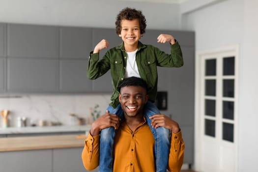 Black father with son on shoulders showing his strength, both smiling