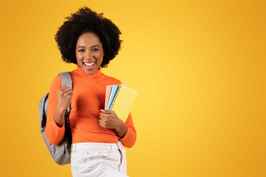 Excited young student with an afro smiling broadly, holding notebooks