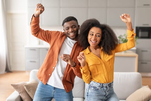 Joyful lovely black couple dancing for fun in their home