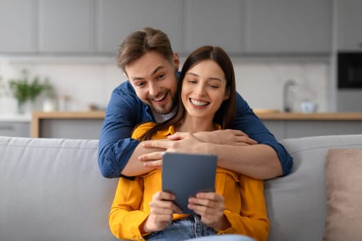 Joyful spouses with digital tablet, man hugging wife from behind