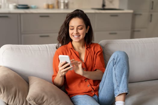 Joyful young woman texting on smartphone at home