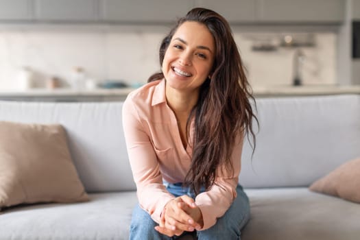 Cheerful woman sitting on grey couch, smiling