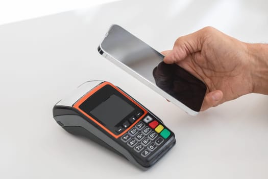 A hand holding a smartphone over a payment terminal, ready to process a contactless mobile payment