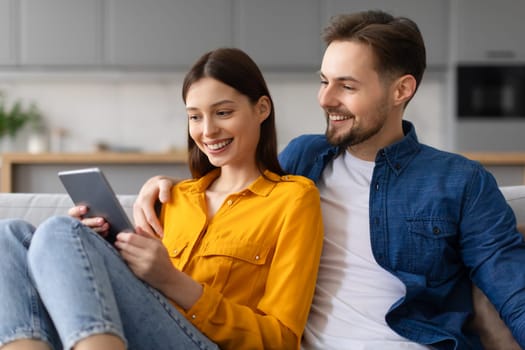 Couple smiling at tablet screen, resting on couch at home