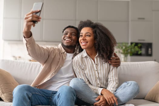 black couple making selfie shot sitting on sofa at home