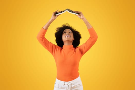Joyful young woman with curly afro hair in an orange turtleneck and white pants