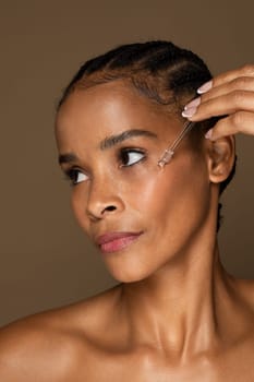 Black middle aged woman using facial serum, closeup