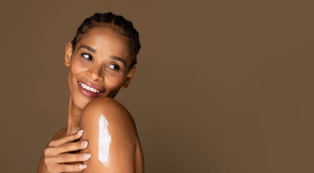 Joyful african american middle aged woman with lotion on shoulder