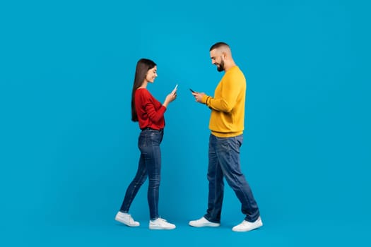 Communication And Technology. Smiling couple using smartphones while walking past each other