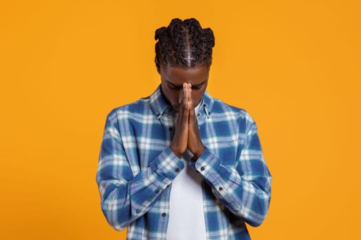 Peaceful young black man in plaid shirt praying with closed eyes