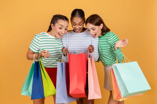 Three amazed multiracial girlfriends looking inside shopping bags