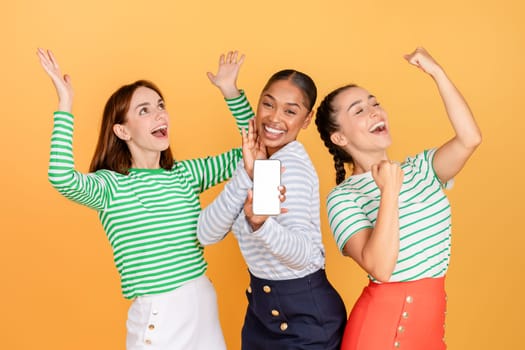 Carefree attractive multicultural millennial ladies showing smartphone with white screen
