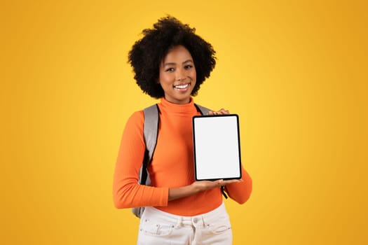 Friendly young woman with a natural afro hairstyle presents a blank tablet screen with a smile