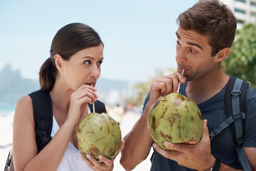 Couple, coconut and drink at beach in summer for vacation with milk, cocktail and juice on journey. People, man and woman with thinking, review and fruit for water, hydration and detox with nutrition.