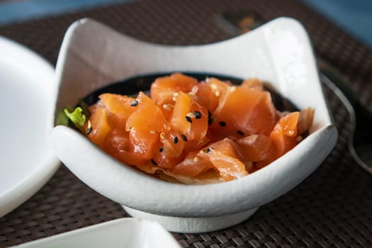 A bowl of salmon tartare with sesame and herbs close up.Healthy vegetarian food, raw salmon meat. Delicious asian dish served on restaurant table
