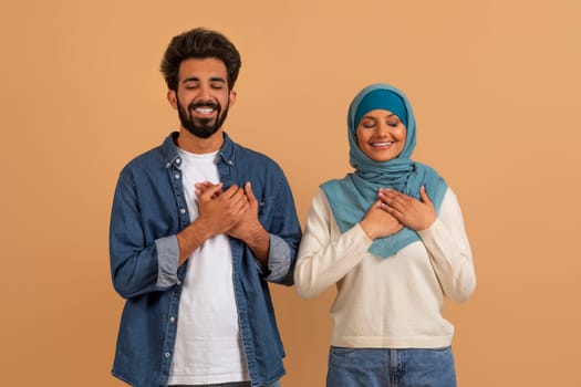 Thankful Muslim Couple Keeping Hands On Chest, Expressing Gratitude Together